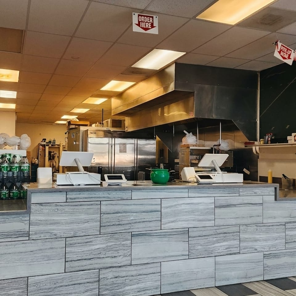 Interior view of a pizza restaurant with a counter, soda bottles, and stacks of pizza boxes.