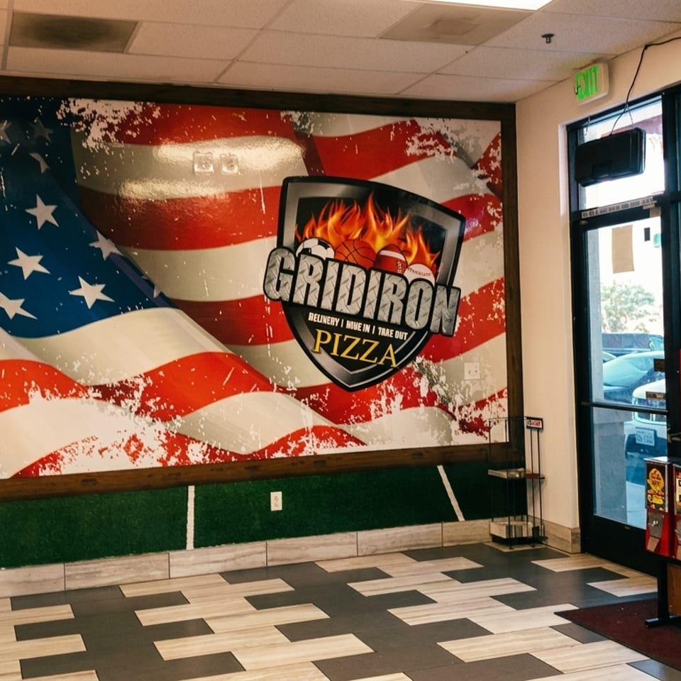 Interior of Gridiron Pizza with a large American flag mural, pizza boxes, and a Coca-Cola fridge.